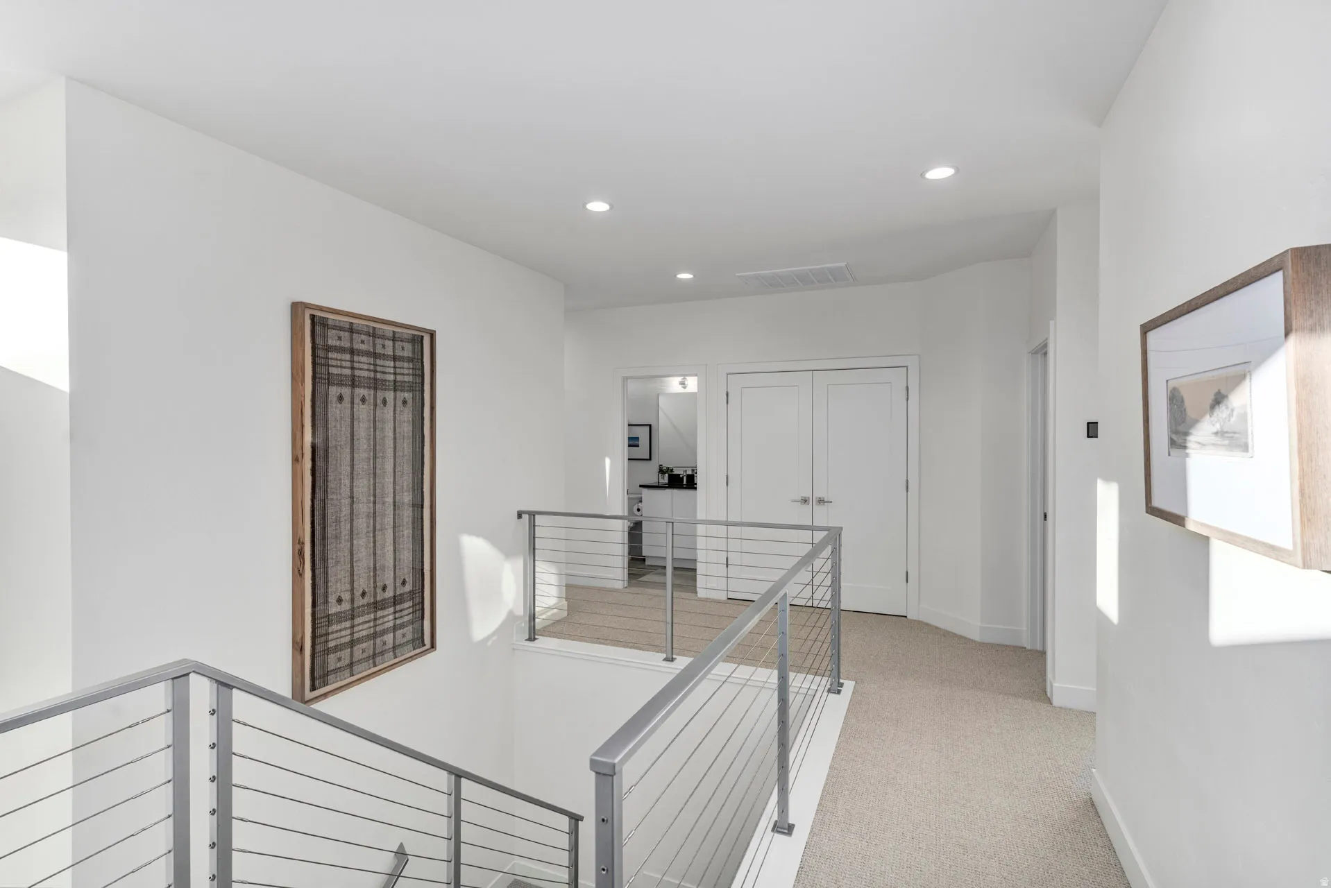 Upper-level hallway with neutral carpeting, recessed ceiling lighting, and contemporary cable railings