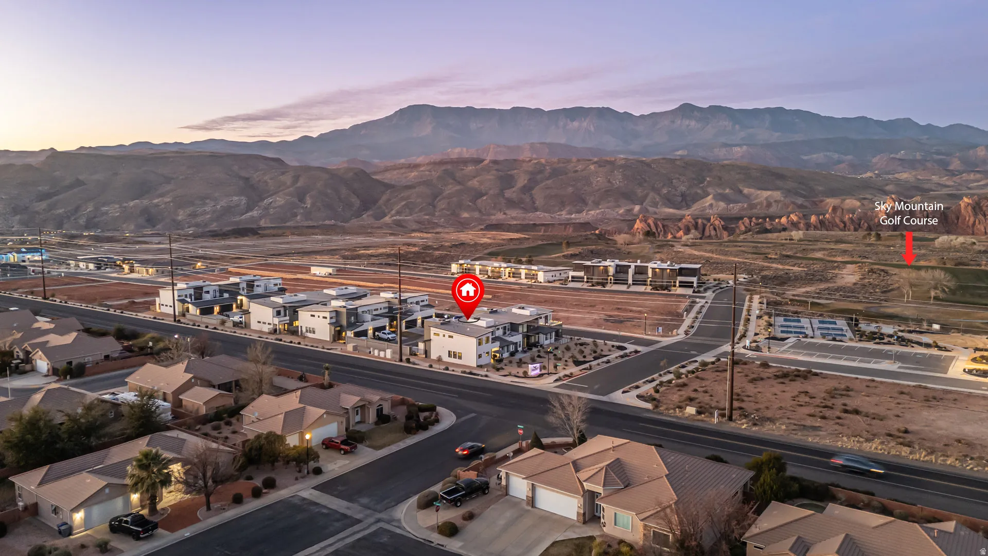 Aerial perspective showcasing the property within a residential development, framed by a mountainous backdrop and Sky Mountain Golf Course.