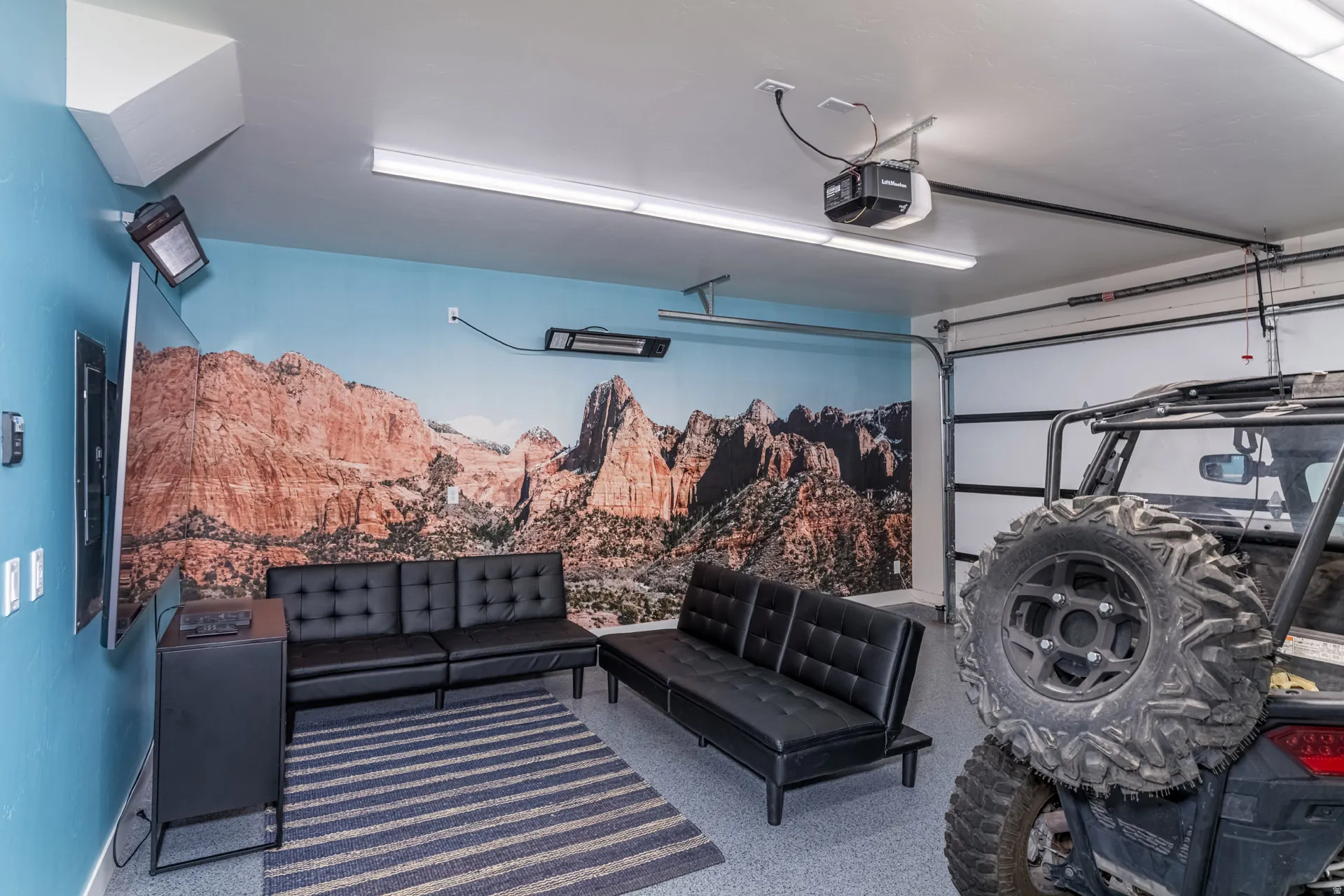 Finished garage space featuring a decorative wall mural, overhead fluorescent lighting, and a wall-mounted heater