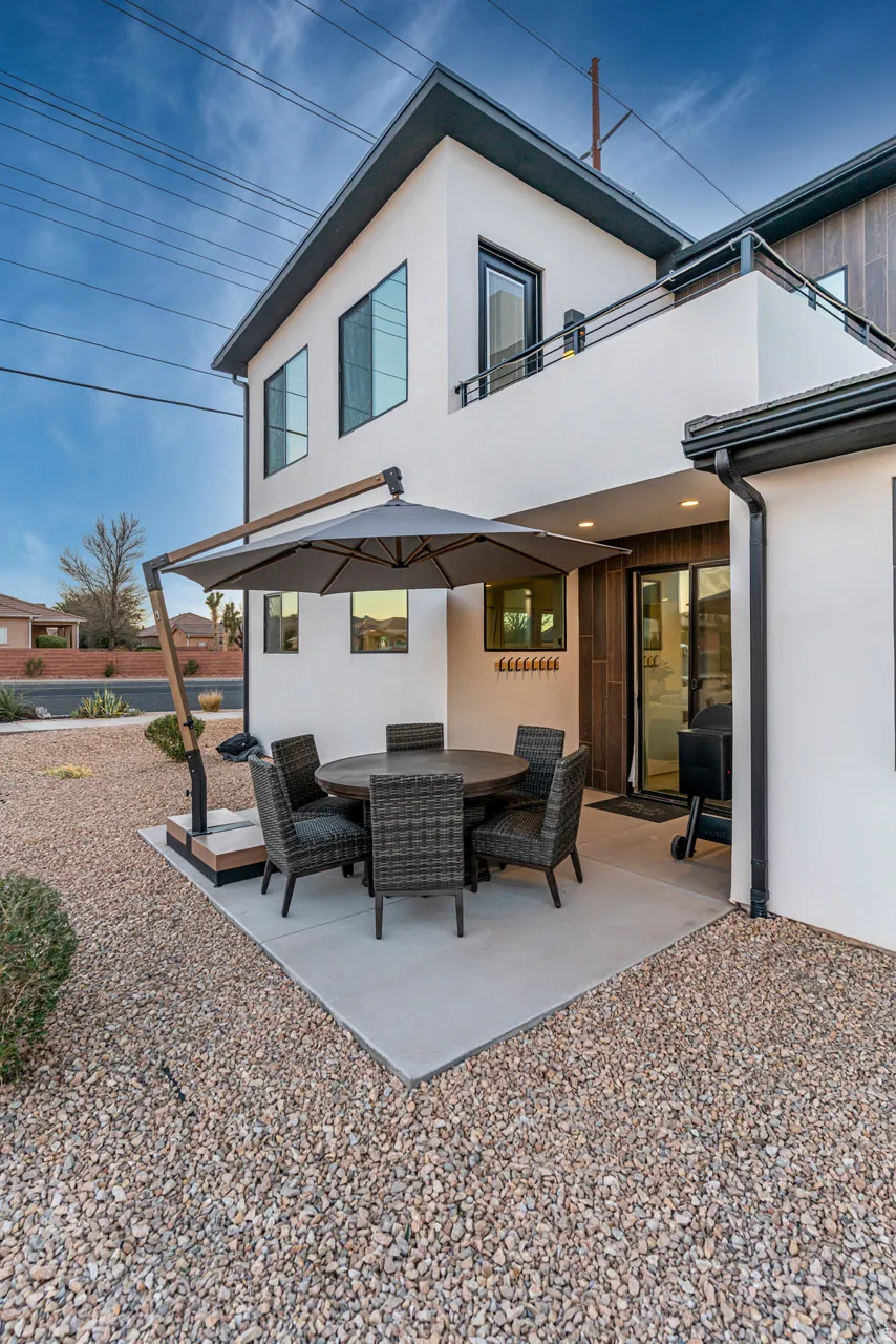Modern two-story exterior featuring white stucco, dark trim, and a second-story balcony with metal railing