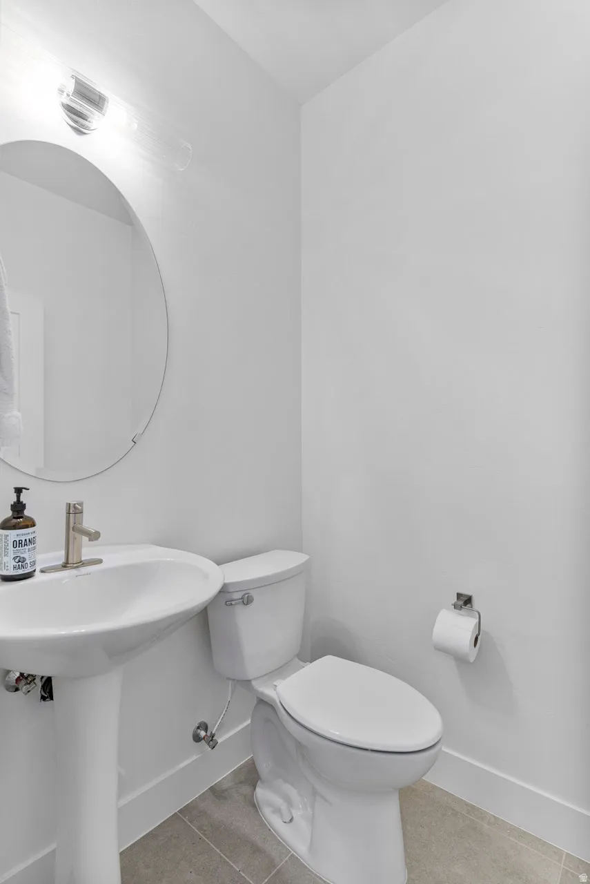 Modern powder room featuring a white pedestal sink, circular mirror, and sleek wall-mounted lighting