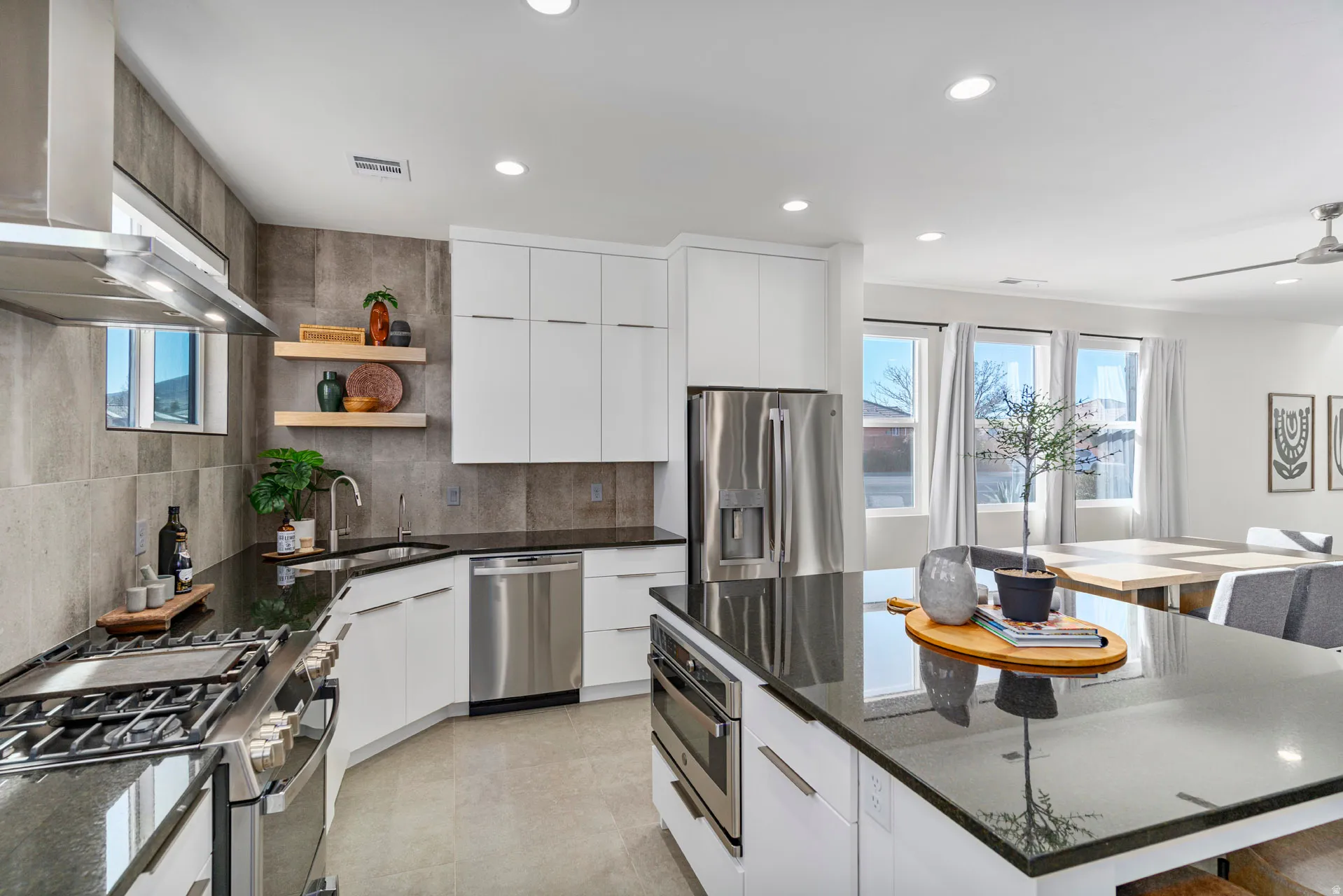 Modern kitchen featuring white cabinetry, black countertops, stainless steel appliances, and a tiled backsplash
