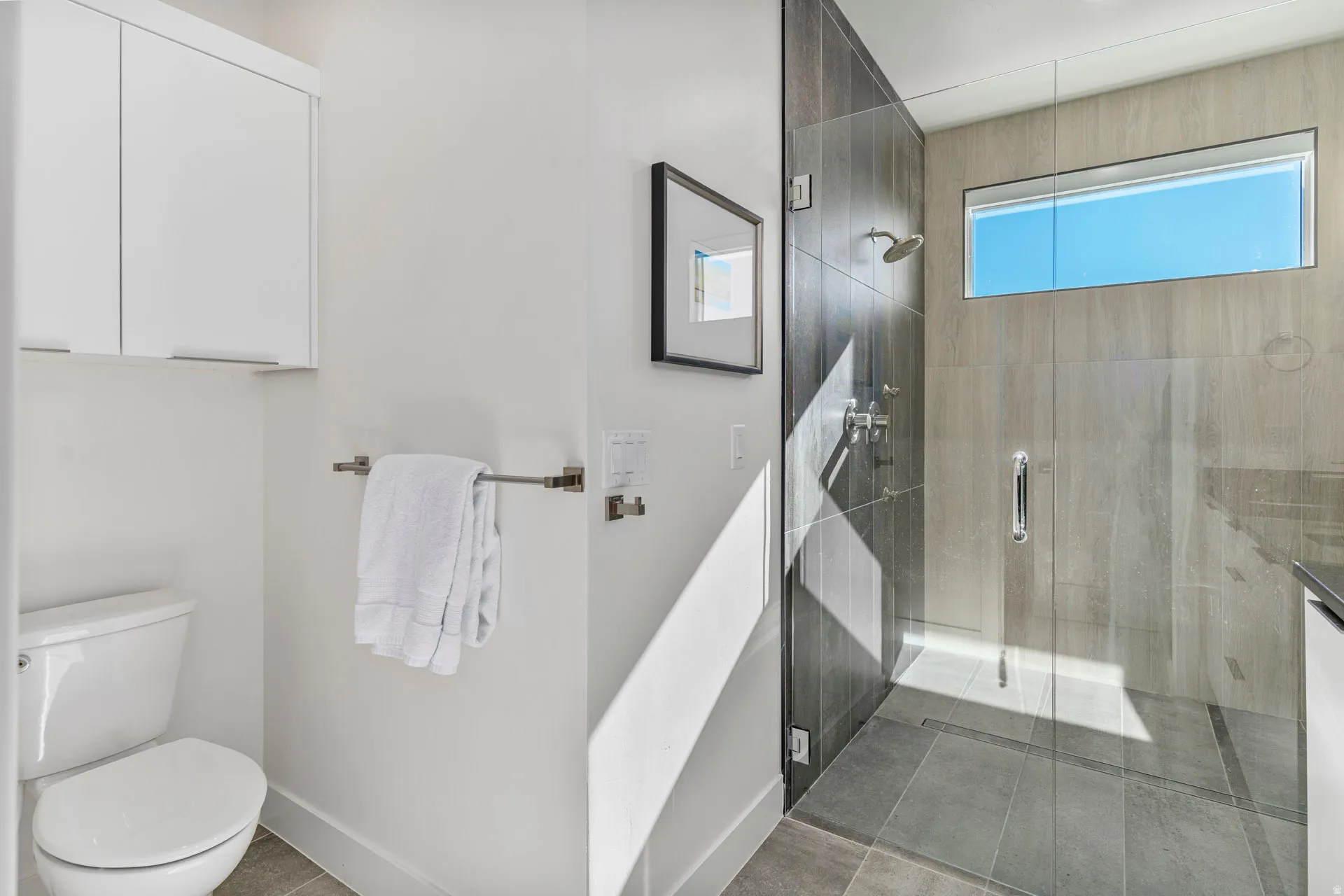 Primary bathroom featuring a frameless glass shower enclosure, a rectangular horizontal window, and a built-in wall cabinet