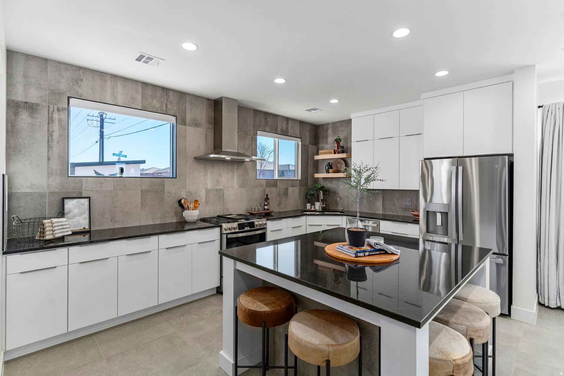 Contemporary kitchen featuring an oversized island with dark stone countertop, white flat-panel cabinetry, stainless steel appliances, and a full-height stone tile backsplash