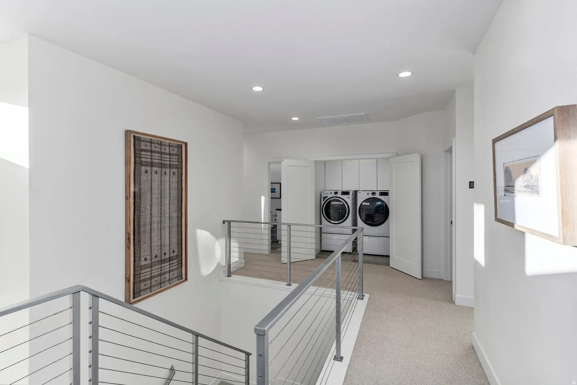 Upper-level laundry closet featuring stacked front-loading washer and dryer units, white cabinetry, and bi-fold doors