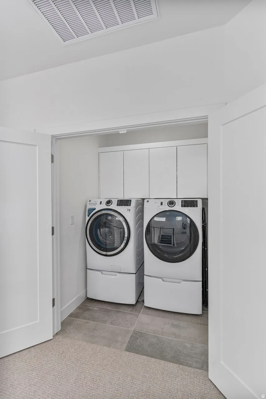 Dedicated laundry area featuring modern front-loading appliances, white cabinetry, and large format tile flooring