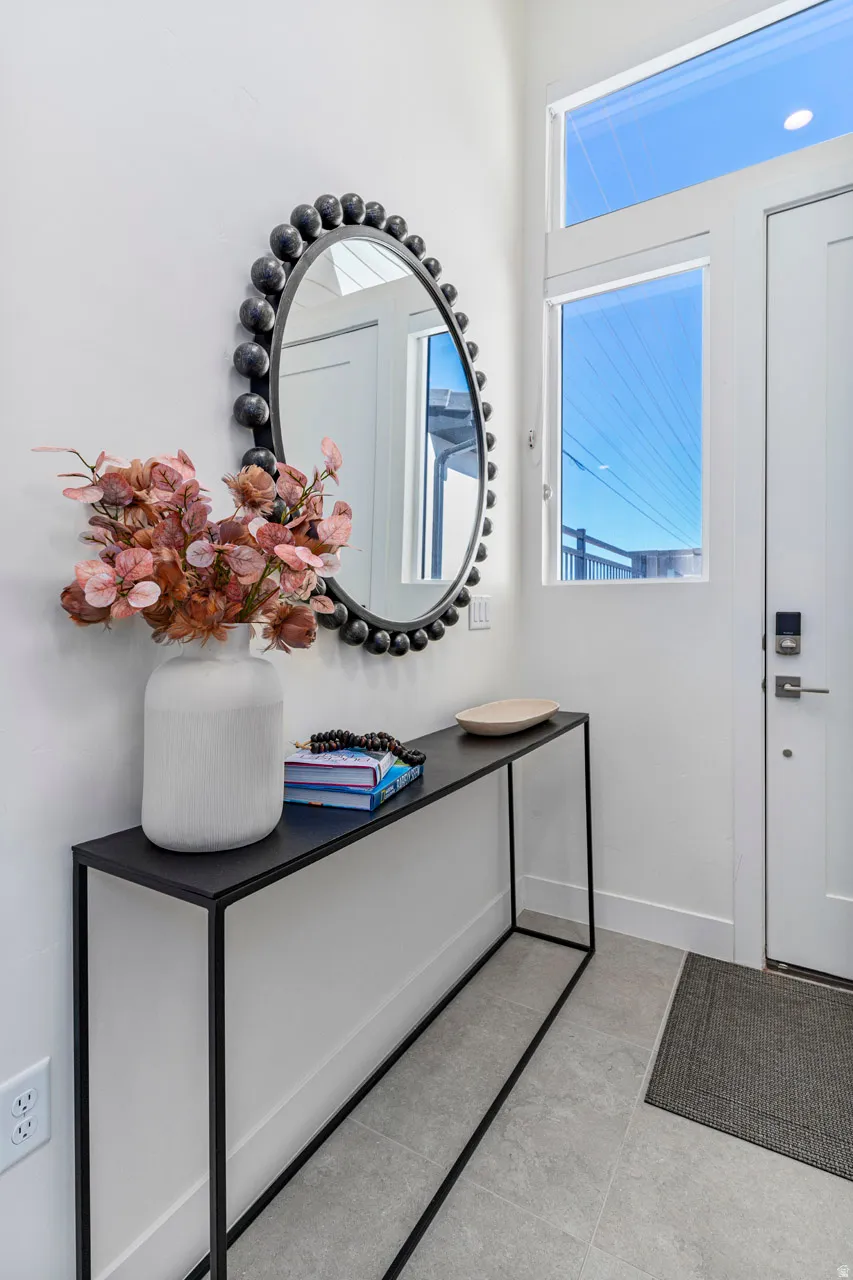 Entryway featuring a contemporary console table, an oval wall mirror with a textured frame, and light-toned tile flooring