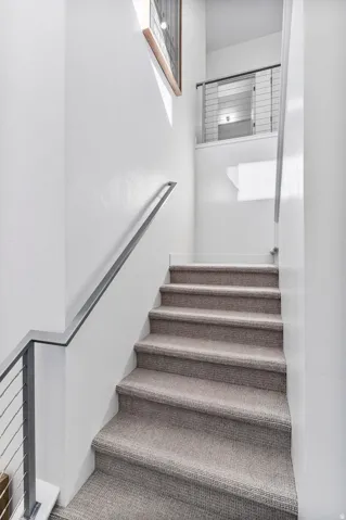 Upgraded textured carpeted staircase featuring a cable railing system and contemporary metal handrail