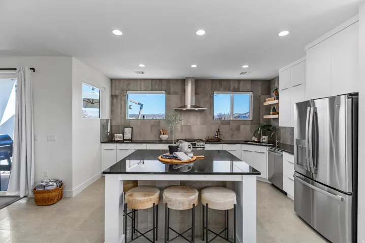 Modern kitchen featuring a black countertop island, stainless steel appliances, white cabinetry, and a textured tile backsplash