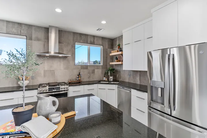 Modern kitchen featuring a stainless steel appliance suite, white cabinetry, dark countertops, and a gray tiled backsplash