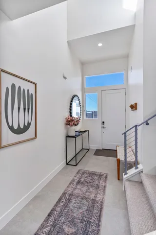 Entryway featuring a high ceiling, transom window, recessed lighting, tile flooring, and carpeted stairs with a metal railing