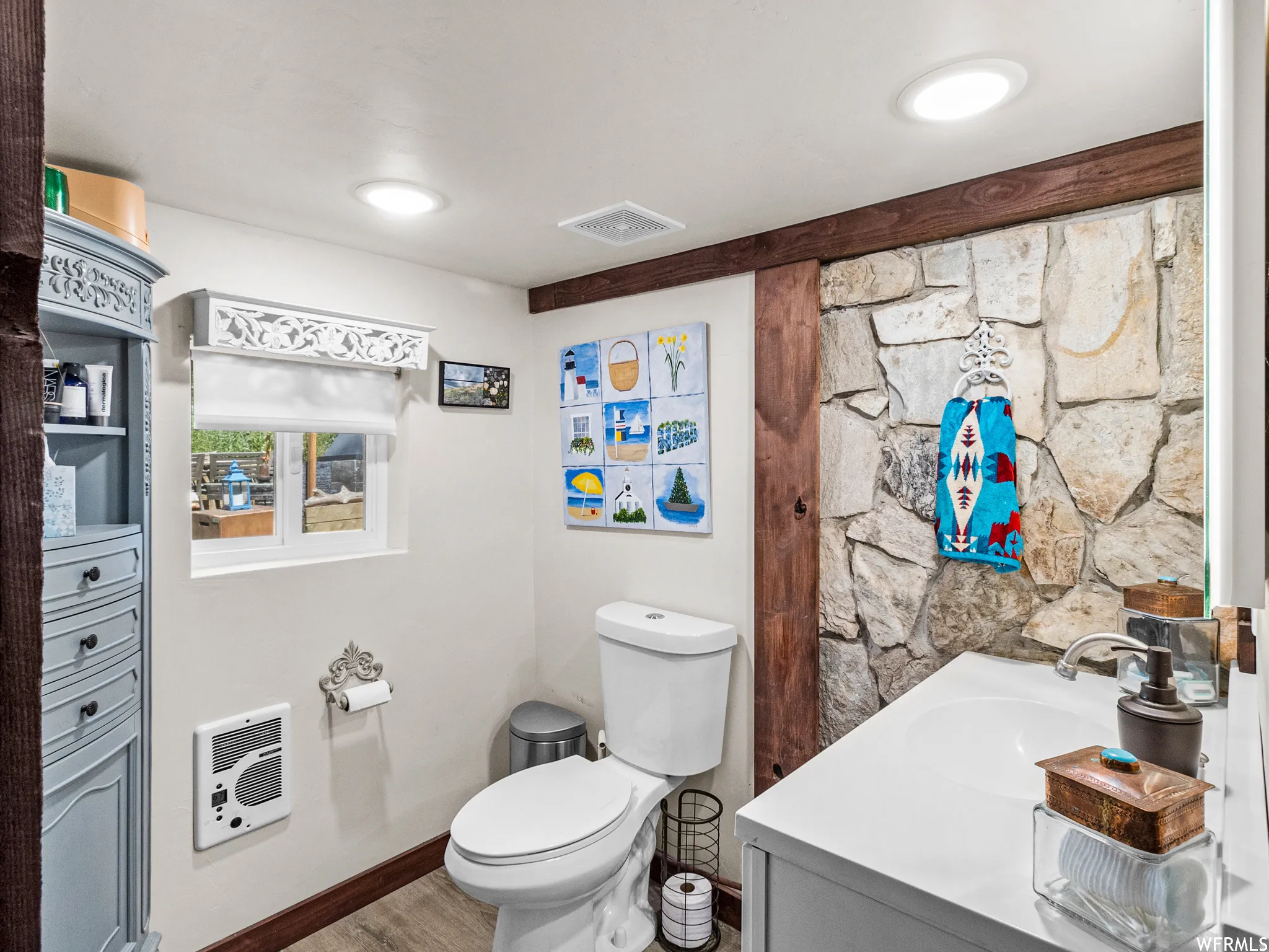 Bathroom featuring a stone accent wall, wood-finish flooring, white vanity with integrated sink, and recessed ceiling lighting