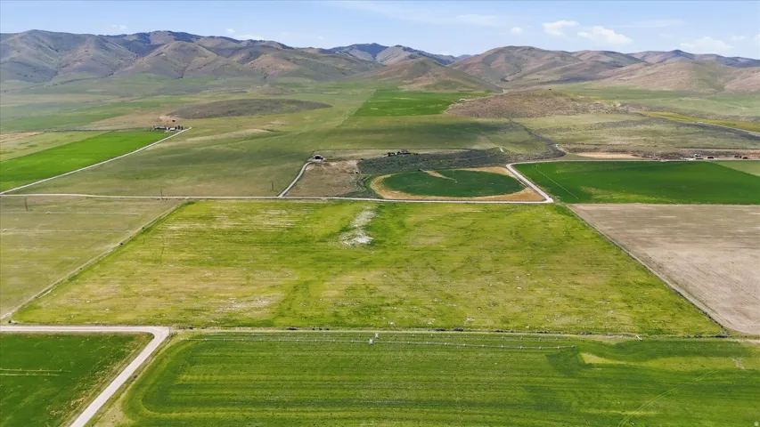 Expansive agricultural land featuring a variety of cultivated fields, dirt access roads, and distant mountain ranges