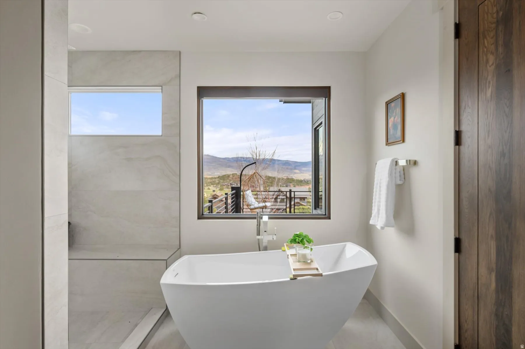 Freestanding soaking tub centered under a large picture window with mountain views.
