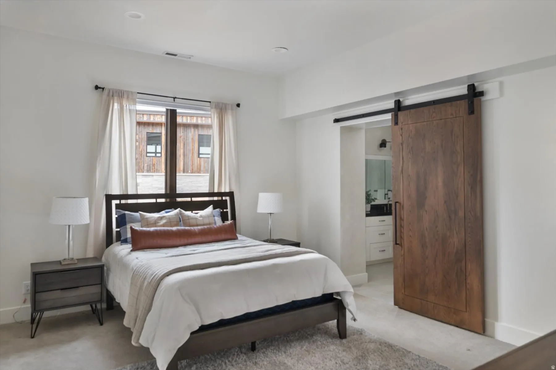 Bedroom with a natural wood barn door, recessed lighting.