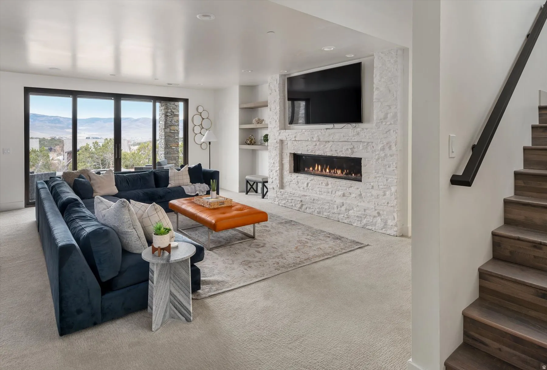 Spacious living area featuring a stone-clad fireplace with built-in linear firebox, flush-mounted television, and a wall of glass sliding doors