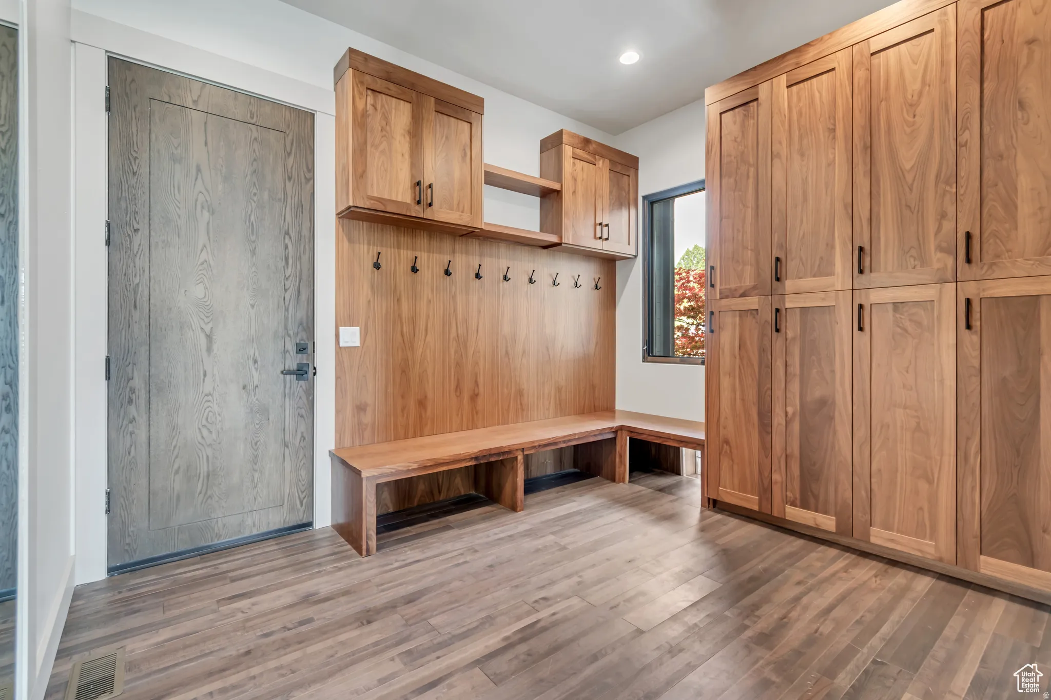Built-in mudroom featuring wood-finish flooring, integrated bench seating, wall-mounted hooks, and overhead cabinetry