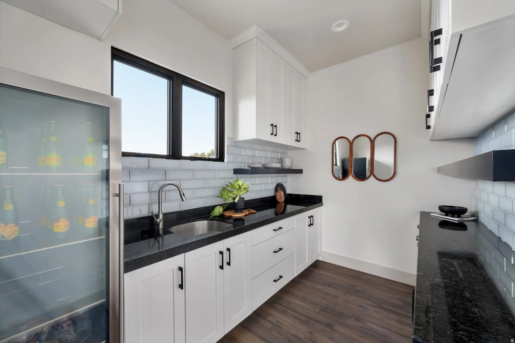 Wet bar featuring white shaker-style cabinetry, black countertops, and a subway tile backsplash