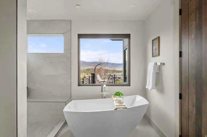 Freestanding soaking tub centered under a large picture window with mountain views.
