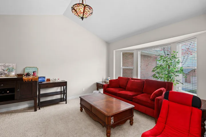 Living area featuring a vaulted ceiling with an ornate semi-flush mount light fixture, plush carpeting, and a bay window