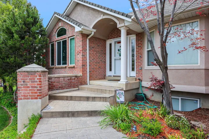 Brick and stucco exterior featuring a covered entry, arched window detailing, stepped concrete pathway, and mature landscaping