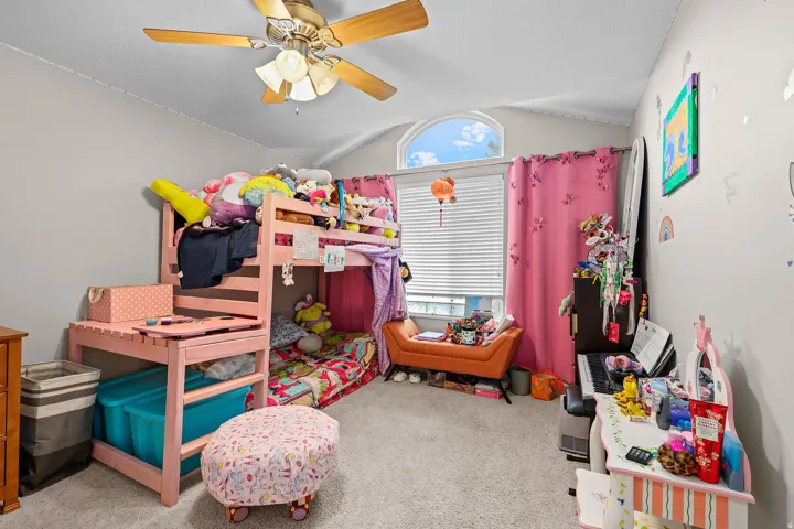 Carpeted room featuring a ceiling fan, vaulted ceiling, and a prominent arched window
