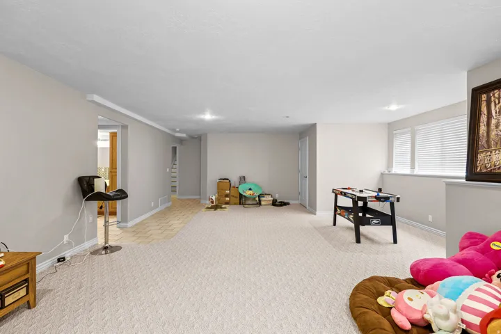 Spacious lower-level area featuring recessed lighting, a combination of patterned carpeting and wood-finish flooring, and multiple windows with blinds