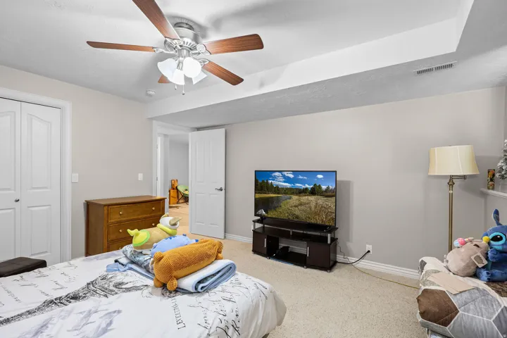 Carpeted room featuring a ceiling fan with integrated lighting, a double-door closet with white panel doors, and a recessed ceiling section