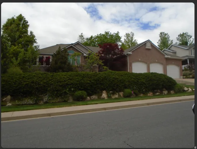 Brick exterior with a three-car garage, arched garage doors, and a manicured hedge