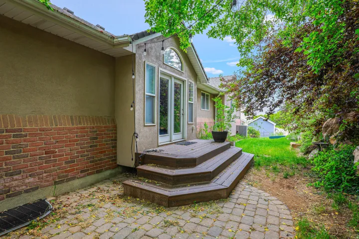 Rear exterior featuring a brick foundation with stucco siding, a multi-tiered wood-finish deck, and a paver patio area