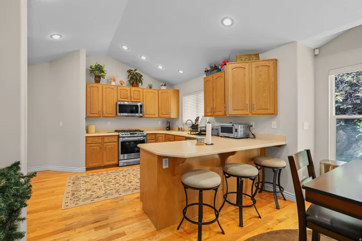 Kitchen featuring warm wood cabinetry, stainless steel appliances, a breakfast bar, recessed lighting, and wood-finish flooring
