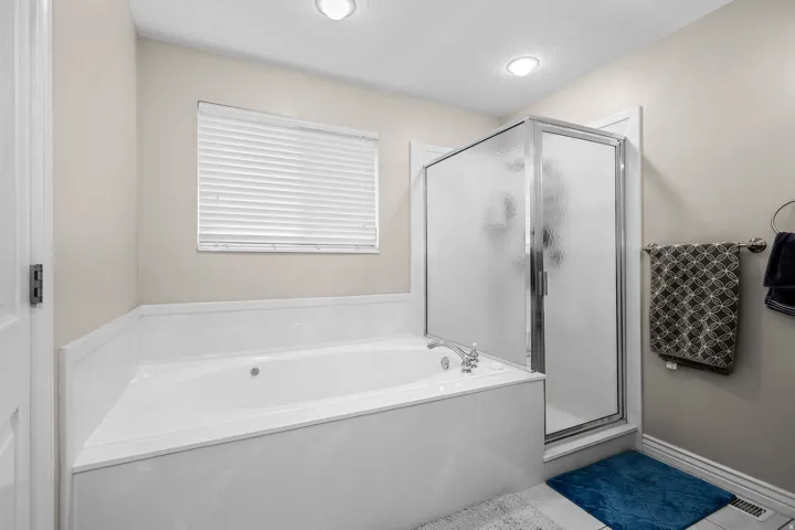 Bathroom featuring a built-in soaking tub with deck-mounted faucet, a separate glass-enclosed shower, and a window with blinds