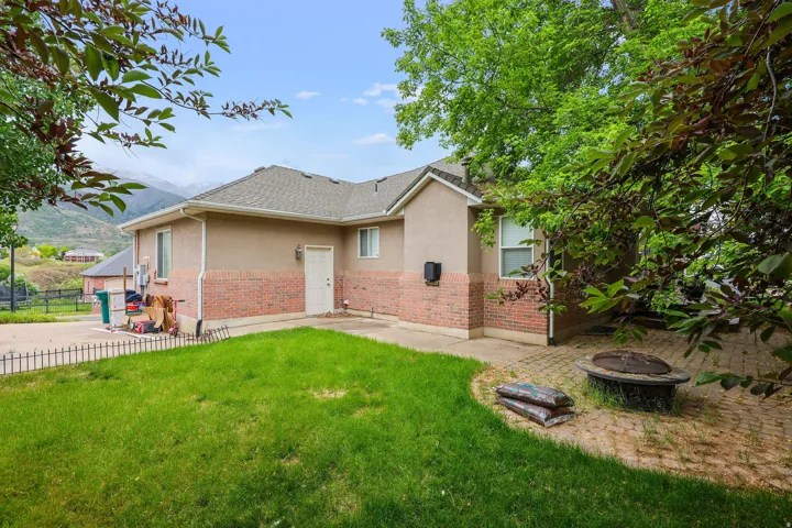 Two-story property featuring a stucco and brick exterior, a paved patio with an integrated fire pit, and a green lawn