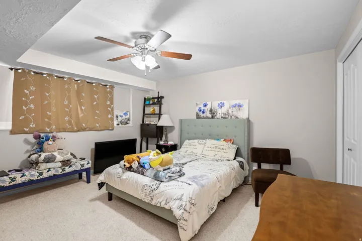 Carpeted room featuring a ceiling fan with light fixture, light-colored walls, and a built-in closet with bifold doors