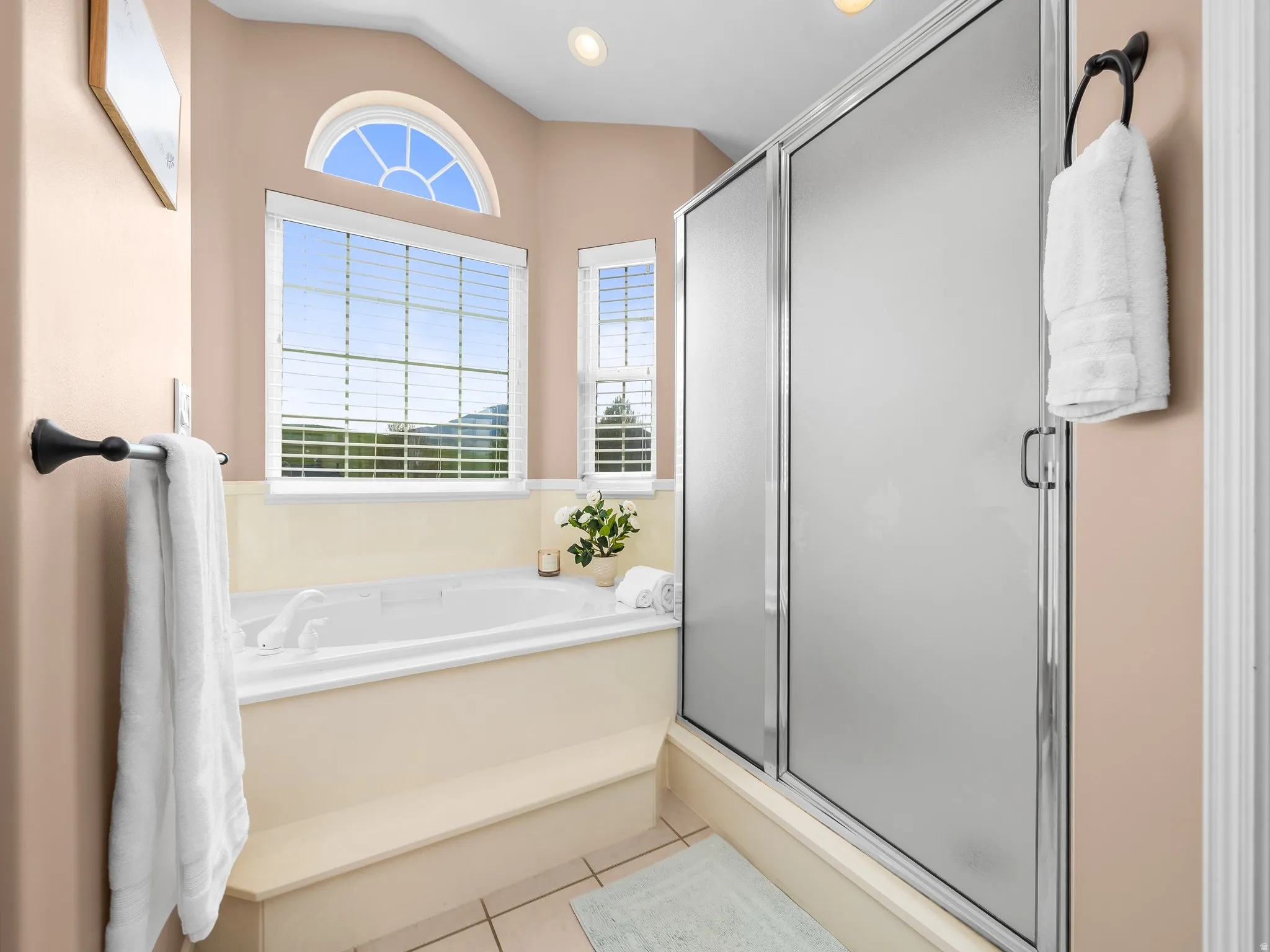 Bathroom featuring a built-in soaking tub with tiled surround, an arched accent window, and a separate shower with frosted glass doors