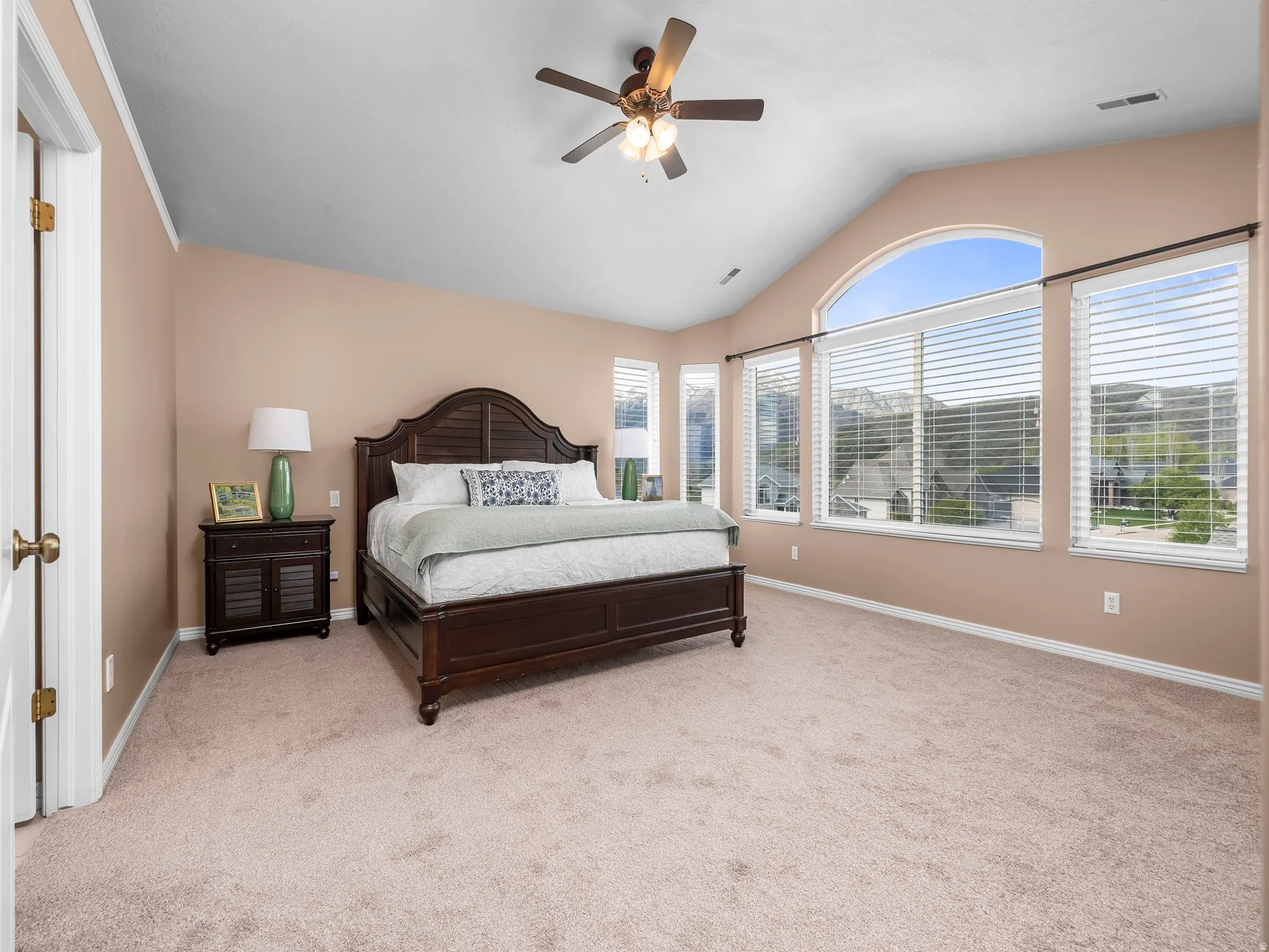 Vaulted ceiling room featuring a large arched window, additional windows with blinds, a ceiling fan, and carpet flooring