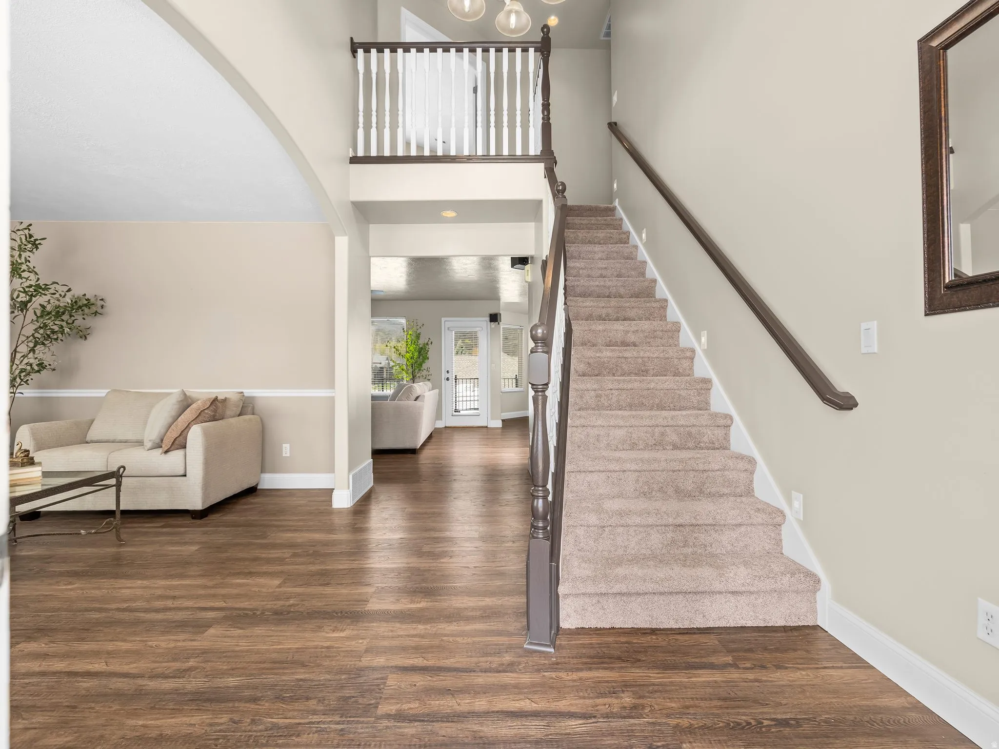 Grand entryway featuring a carpeted staircase with a dark wood handrail and white balusters, wood-finish flooring, and light-toned walls with wainscoting