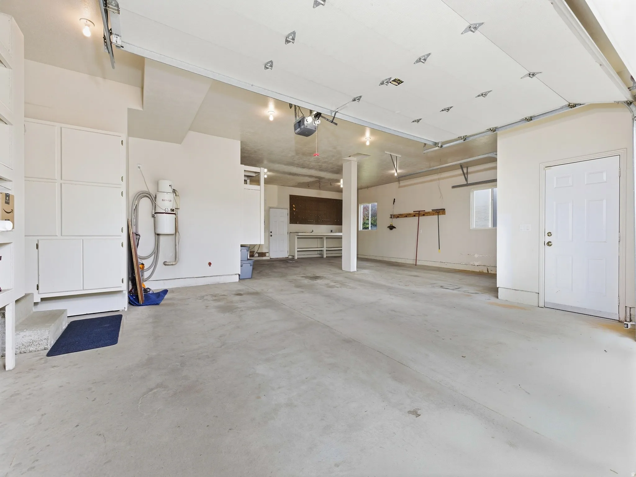 Spacious garage with light-toned concrete flooring, overhead lighting, windows, built-in cabinetry, and a service door