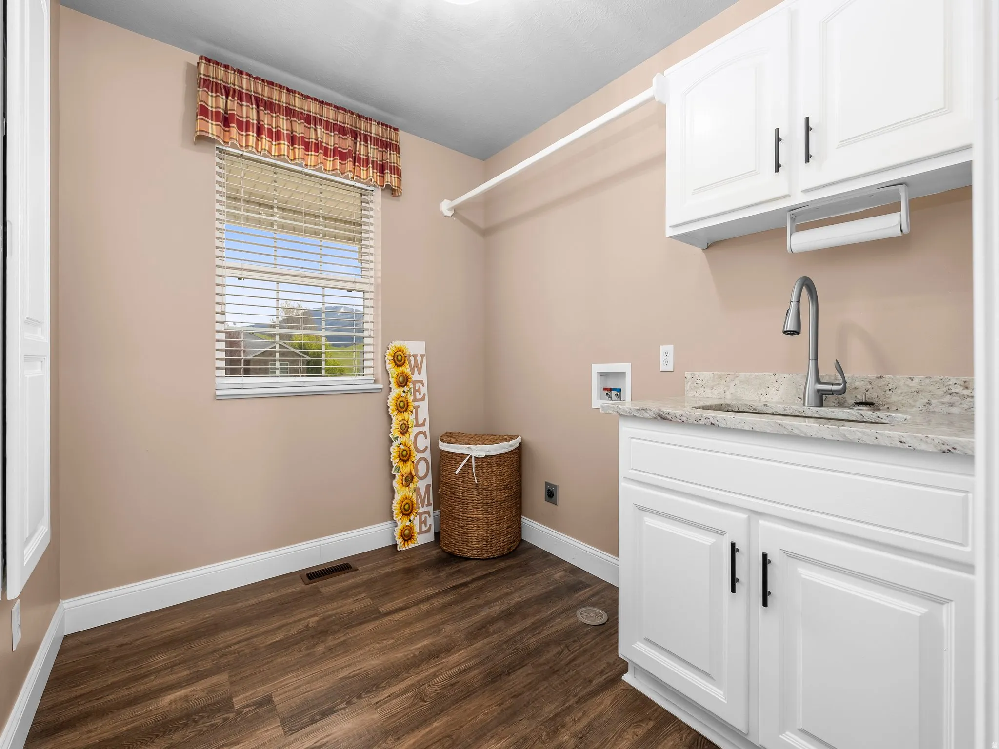 Utility area featuring wood-finish flooring, a single window with blinds, white cabinetry, a light-toned countertop, and a stainless steel sink with a gooseneck faucet