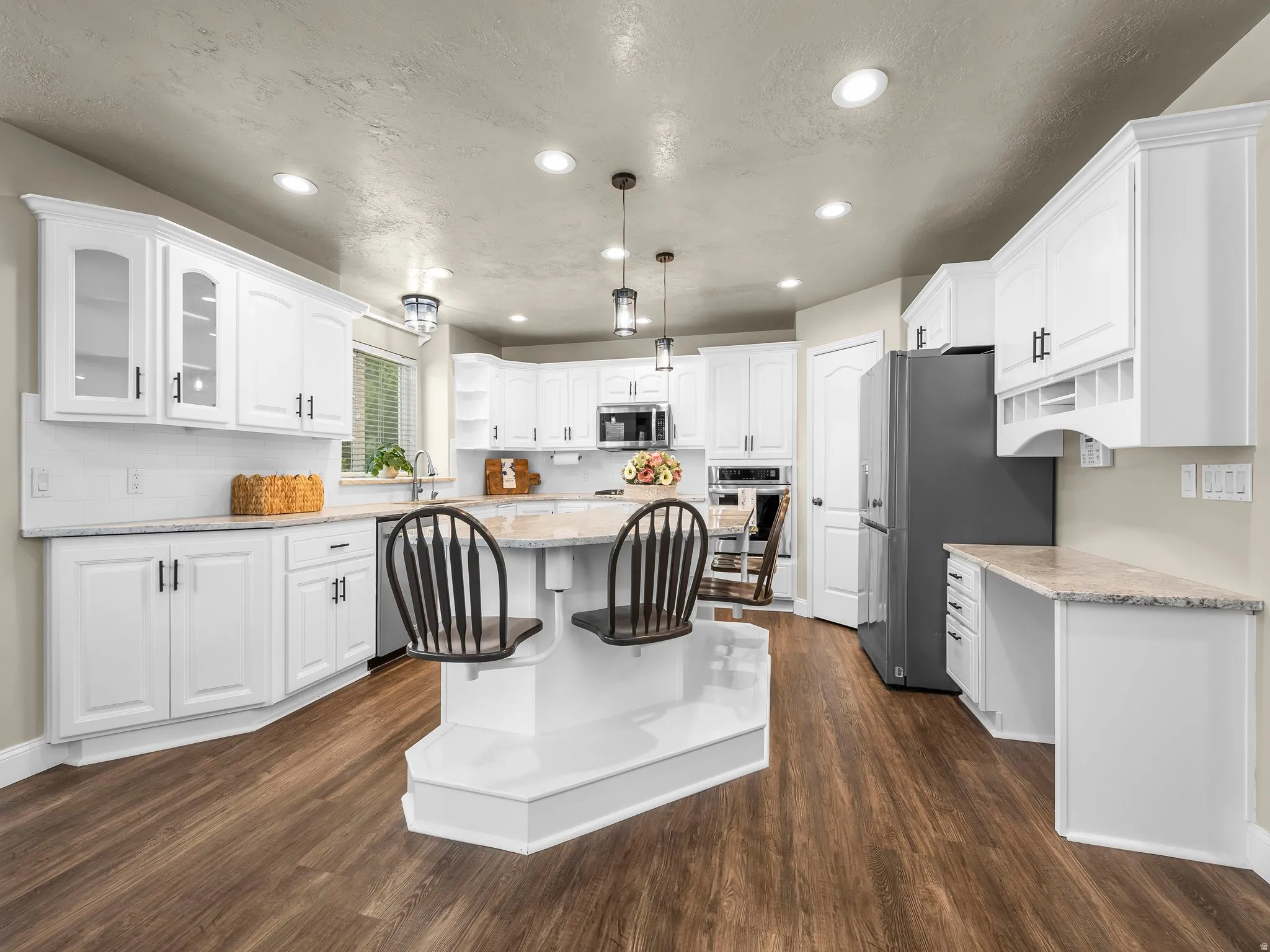 Kitchen featuring a central island with integrated seating, white cabinetry, wood-finish flooring, recessed lighting, and a white subway tile backsplash