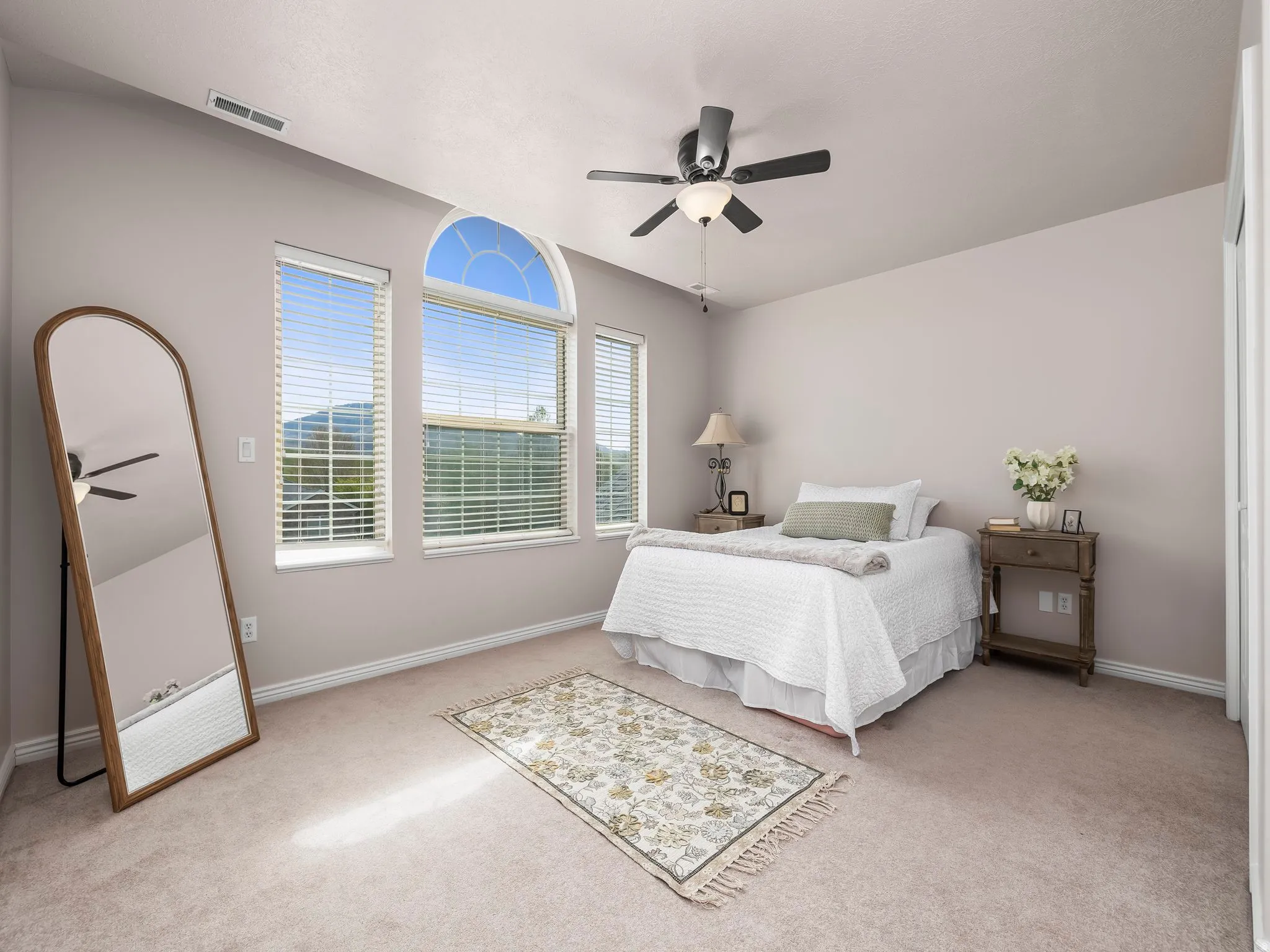 Room featuring three windows with blinds, including an arched transom window, a ceiling fan with integrated lighting, and neutral-toned wall-to-wall carpeting