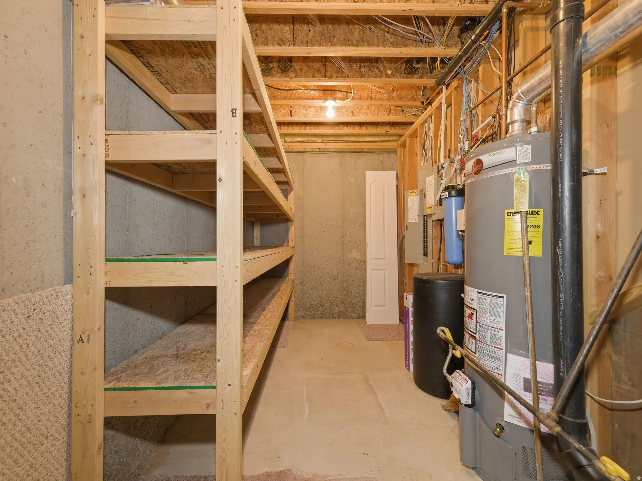 Lower level utility area featuring built-in wood shelving, exposed ceiling joists, concrete flooring, and a water heater