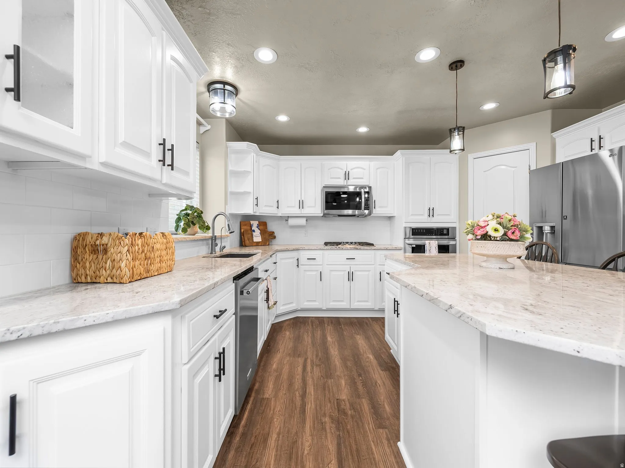 Kitchen featuring white cabinetry with black hardware, light-toned countertops, stainless steel appliances, wood-finish flooring, and pendant lighting