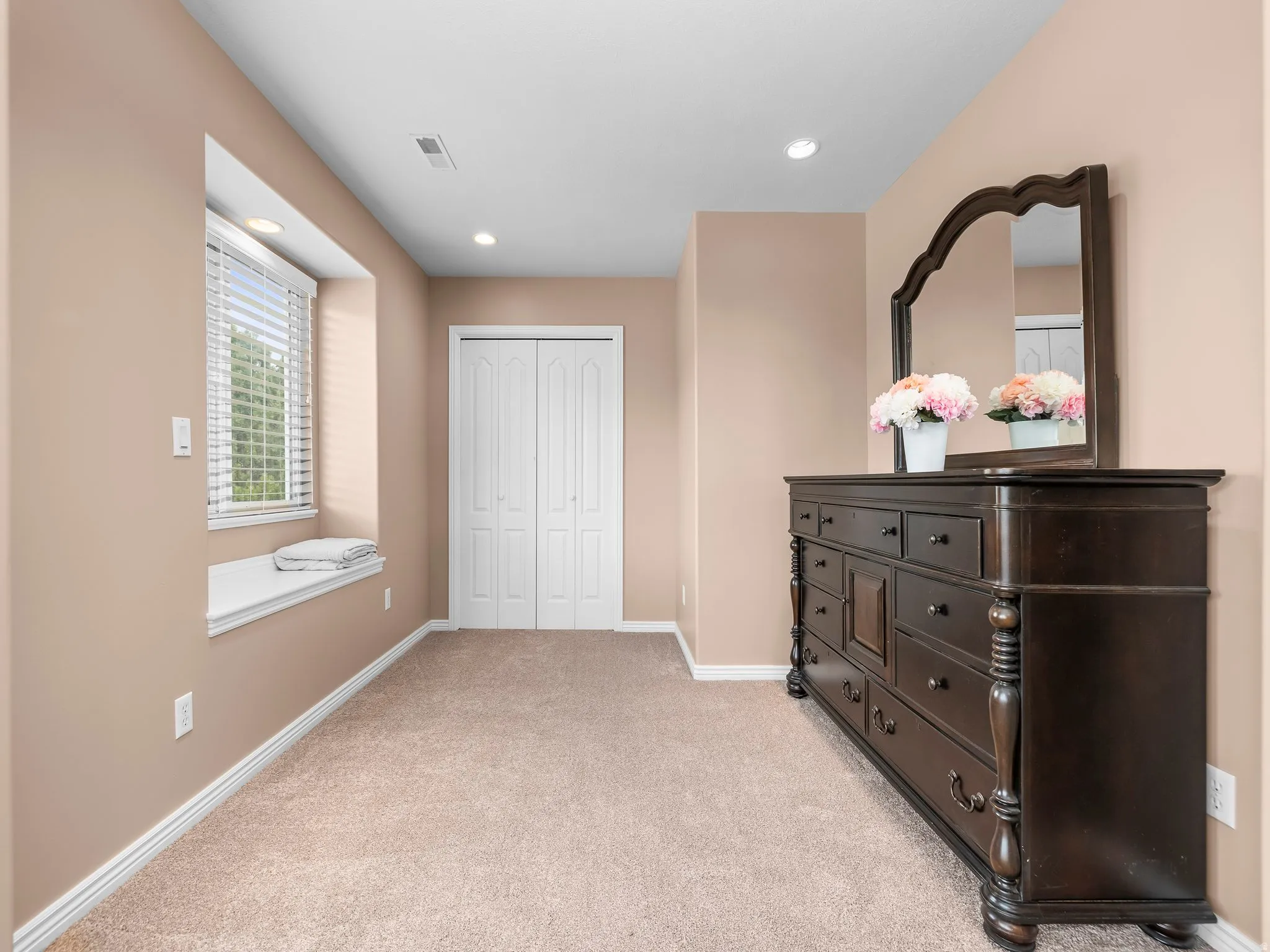 Plush carpeted room featuring a window with built-in bench seating, recessed lighting, and a bi-fold closet