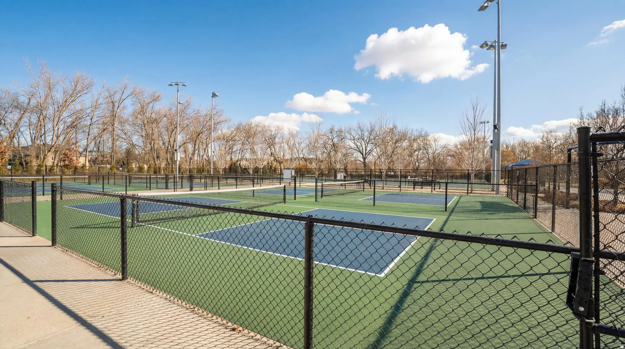 Multiple fenced pickleball courts featuring green and blue surfacing, with overhead lighting visible