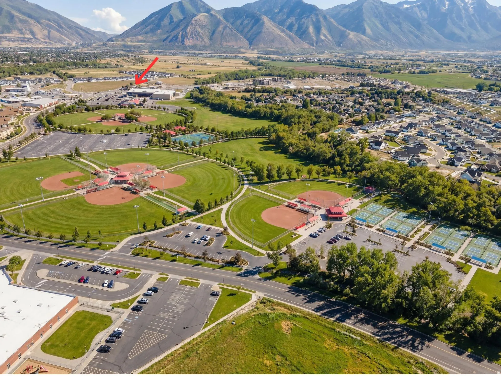 Aerial perspective showcasing a large community park with multiple baseball fields, tennis courts, and ample parking