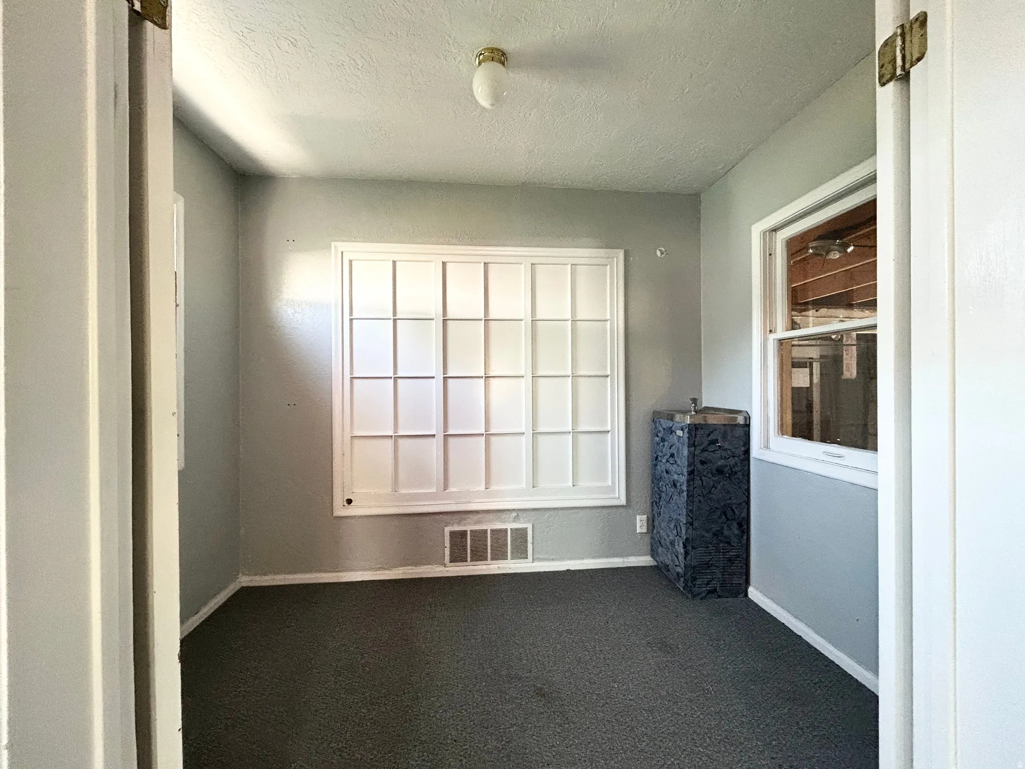 Room featuring a fixed decorative window with grid pattern, wall-mounted light fixture, dark textured flooring, and a built-in cabinet with a dark patterned surface