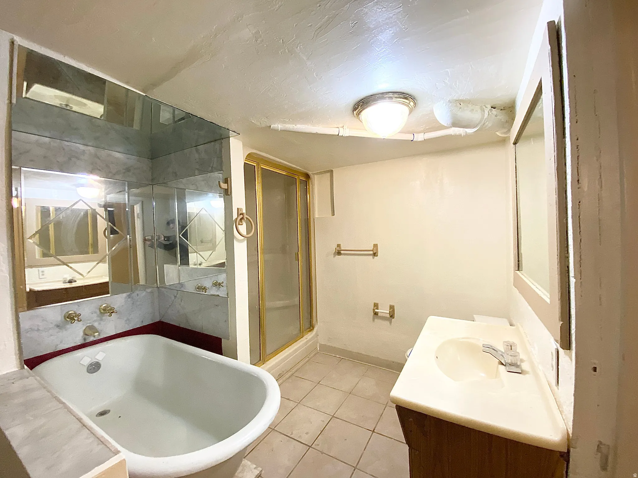 Bathroom featuring a clawfoot tub, mirrored wall accents, a shower enclosure with a gold-tone frame, a vanity with a white countertop, and tile flooring
