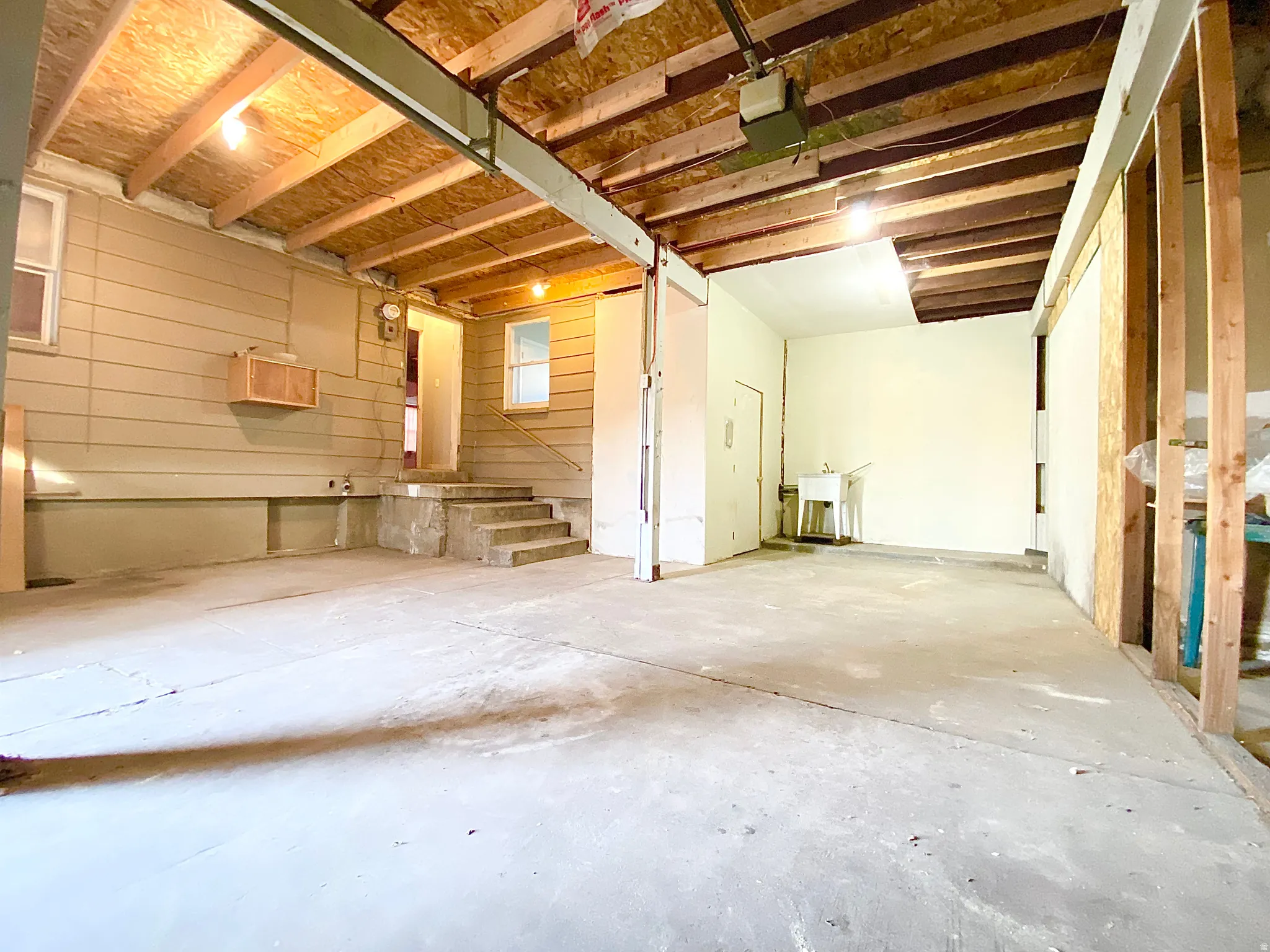 Spacious utility area featuring exposed ceiling joists, concrete flooring, a utility sink, and wall-mounted cabinetry