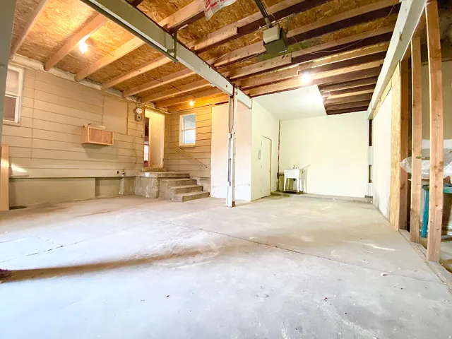 Spacious utility area featuring exposed ceiling joists, concrete flooring, a utility sink, and wall-mounted cabinetry